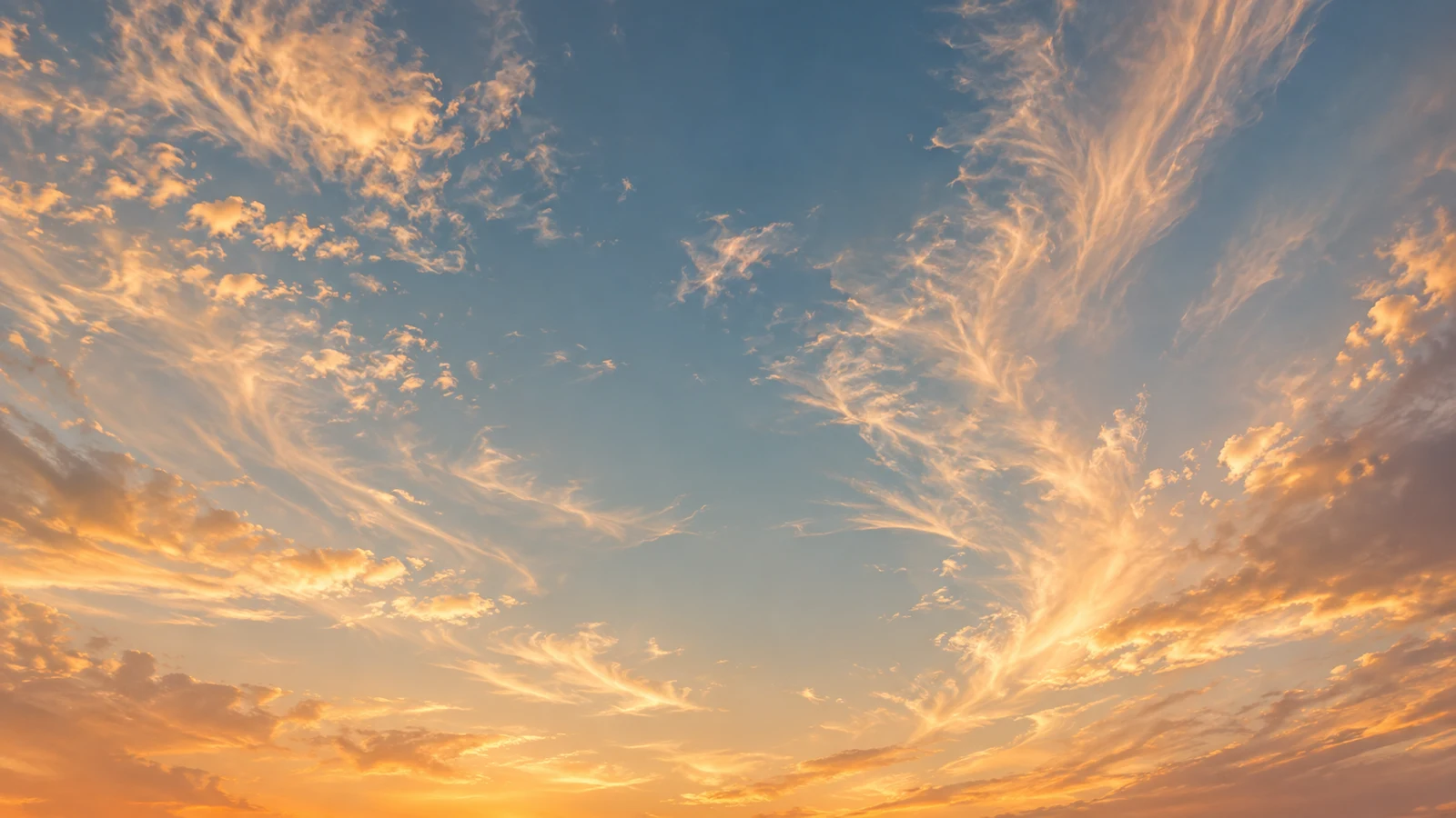 Céu aberto visto de baixo, com nuvens finas douradas e azul ao fundo, no fim da tarde