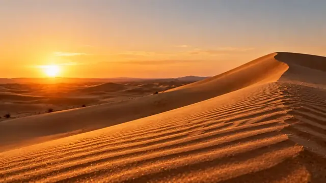 Sand dunes at sunset with wind-carved ripples and an empty horizon under a clear sky